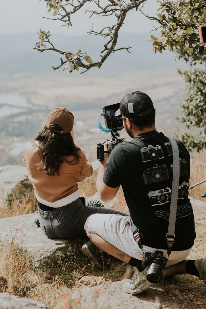 A filmmaking duo captures scenic outdoor views with professional gear on a sunny day.