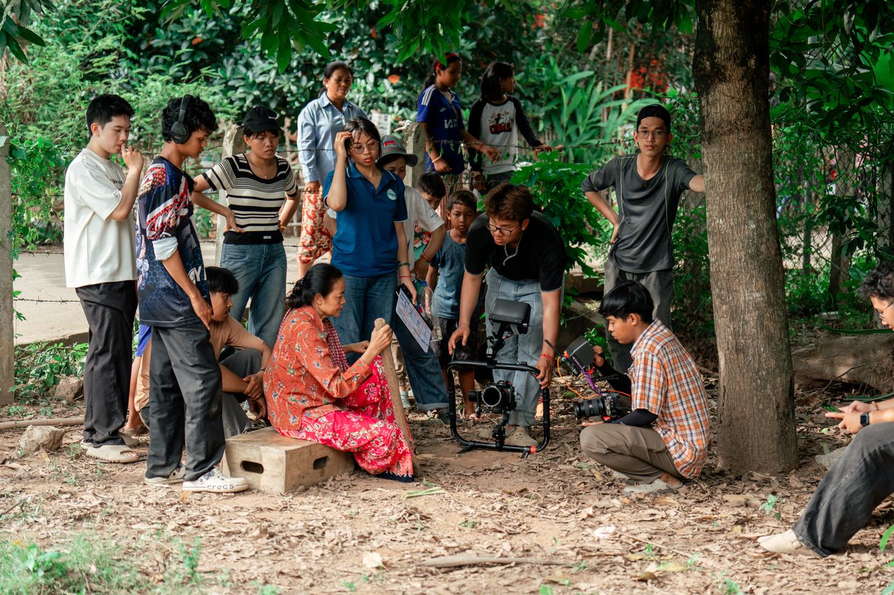 about-us Filmmakers and crew collaborate on outdoor movie set under trees.