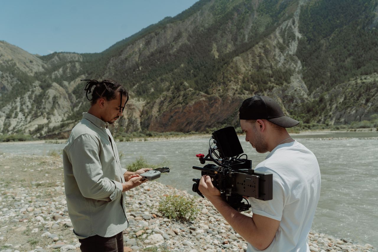 heros-img Two filmmakers capture scenic mountain river with professional camera.