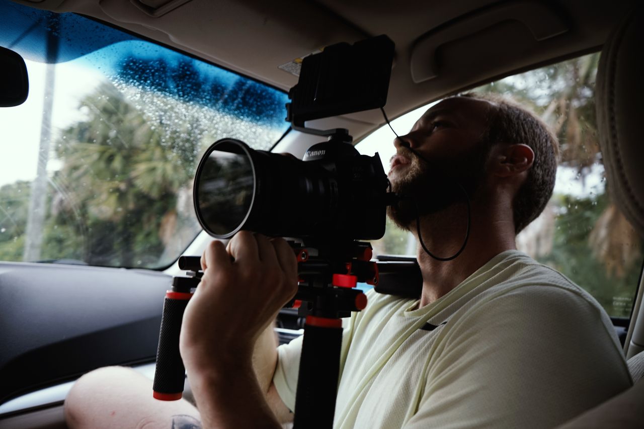 A cinematographer operates a camera rig inside a vehicle for filming.